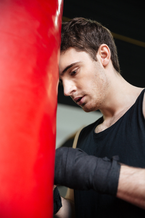 Tired man boxer wearing gloves leaning on red punchbag