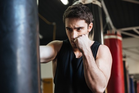 Attentive young boxer kicking punching bag in gymの写真素材