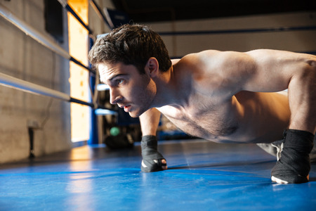 Side view of a concentrated boxer with naked torso doing push ups on boxing ring