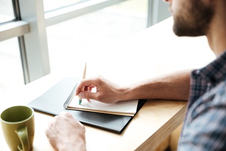 Cropped photo of young man in office coworking while writing notes.