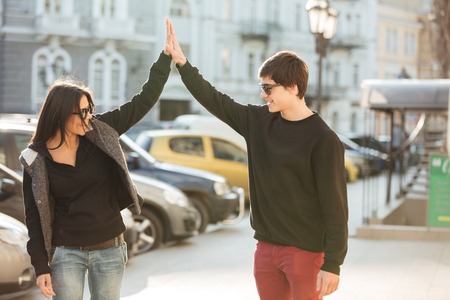 Image of happy young woman walking outdoors with her brother. Looking aside and give a high-five to each other.の写真素材