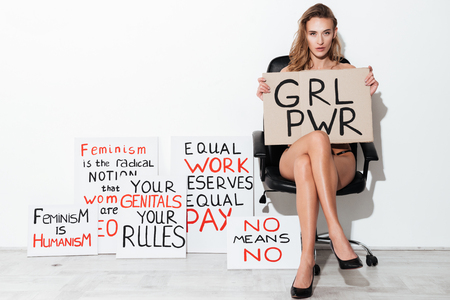 Picture of young woman posing over white wall near blanks with text about feminism. Looking at camera.の写真素材