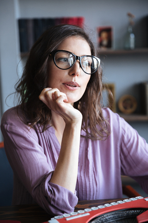 Portrait of a pensive mature authoress in eyeglasses thinking and looking away indoorsの写真素材