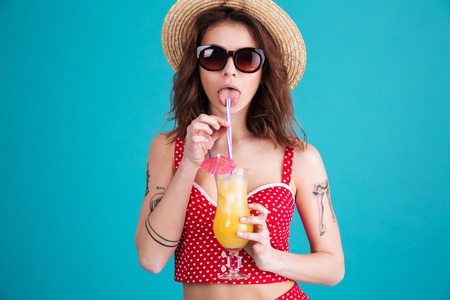 Picture of pretty young lady with cocktail looking at camera isolated over blue background.の写真素材