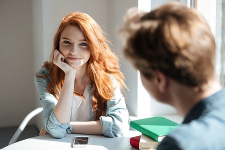 Portrait of cute redhead woman student in cafe against her friendの写真素材