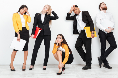 Image of a group of tired colleagues standing isolated with folders in office. Woman looking at camera.の写真素材