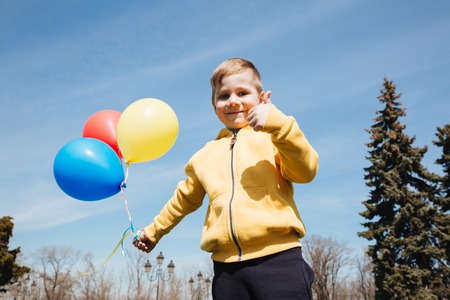 Photo of smiling little children boy walking outdoors in park with balloons. Looking at camera and showing thumbs up.の写真素材