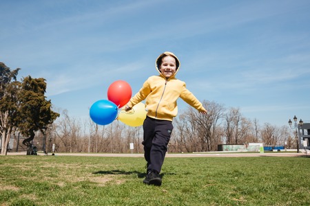 Photo of smiling little children boy walking outdoors in park with balloons. Looking at camera.