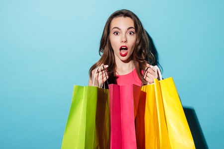 Portrait of a shocked pretty girl holding colorful shopping bags isolated over blue background