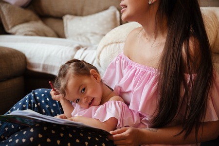 Image of young mother with her little daughter sitting on floor indoors drawing in colouring book. Looking aside.の写真素材