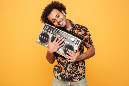 Image of young smiling african man standing with tape recorder isolated over yellow background. Looking at camera.の写真素材