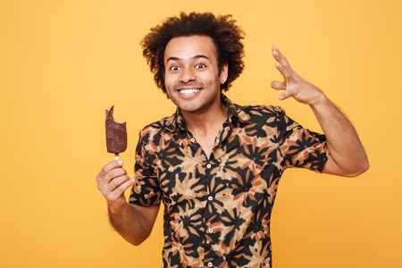 Portrait of a happy smiling afro american man holding ice cream isolated over yellow backgroundの写真素材