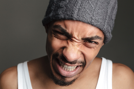 Picture of young emotional african man isolated over grey background. Looking at camera.