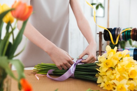 Cropped image of woman florist using ribbon to bandage bouquet of yellow flowers in workshopの写真素材