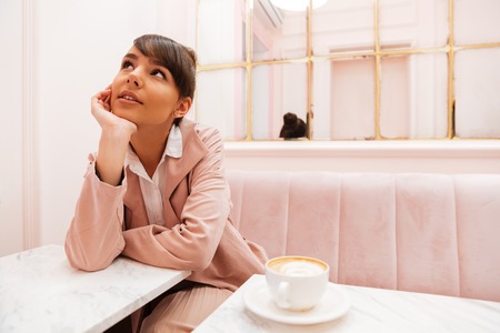 Portrait of a pretty young woman sitting and looking away at cafe tableの写真素材