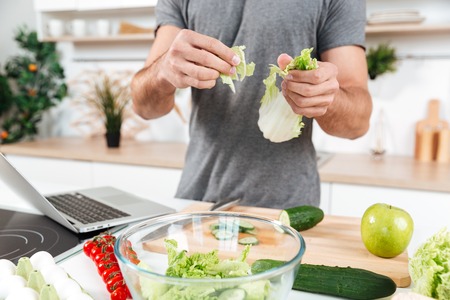 Cropped image of a man cooking salad in the kitchen with laptopの写真素材