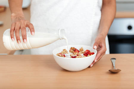 Cropped image of young african woman dressed in towel standing at home and eating strawberry with muesli.の写真素材