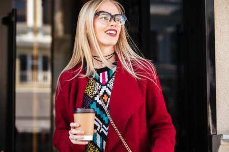 Image of attractive young caucasian woman walking outdoors. Looking aside drinking coffee.の写真素材