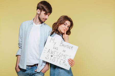 Picture of happy brother and sister showing nameplate over yellow background. Looking camera.の写真素材