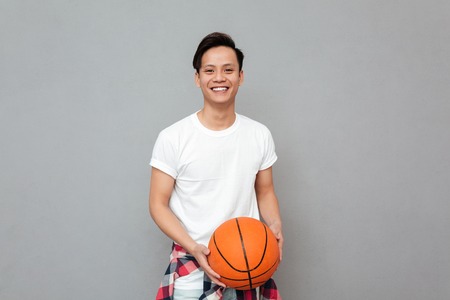 Image of happy young asian man over grey background with basket ball. Looking at camera.の写真素材
