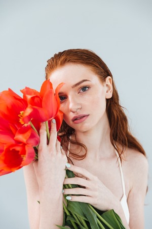 Fashion portrait of a beautiful redheaded woman holding tulip flowers and looking at camera isolatedの写真素材