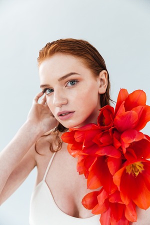 Fashion portrait of a young sensual redheaded woman holding tulip flowers and looking at camera isolatedの写真素材