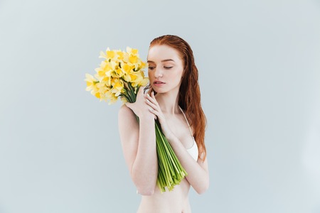 Fashion portrait of a young redheaded woman holding narcisuss flowers and posing isolatedの写真素材