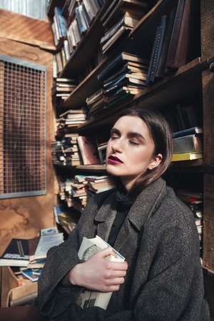 Portrait of a beautiful young girl in coat holding book in an old libraryの写真素材