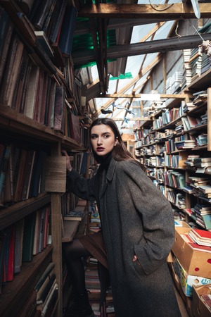 Portrait of a fashionable young woman choosing book from a shelf in a warehouseの写真素材