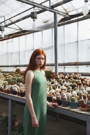 Portrait of a young redheaded girl standing in a glass house and looking at cameraの写真素材