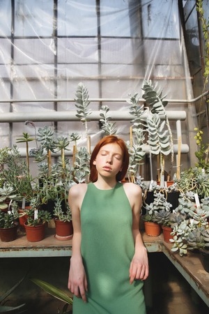 Portrait of an attractive redheaded girl standing in a glass house with eyes closedの写真素材