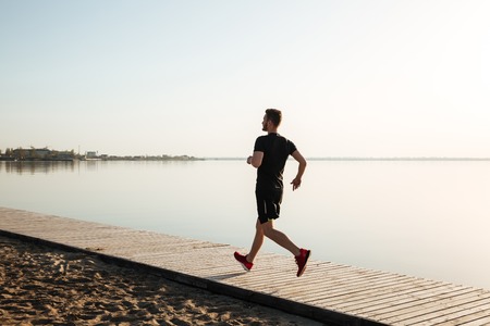 Back view full length portrait of a healthy sportsman running on the beach in the morningの写真素材