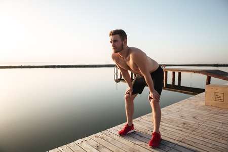 Portrait of a young healthy sportsman resting after jogging outdoors at the beach