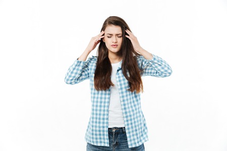 Portrait of a young casual woman suffering from migraine and keeping hands on her head isolated over white backgroundの写真素材