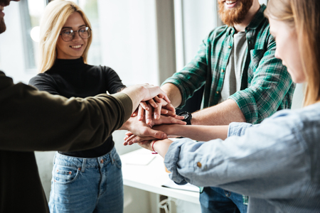 Image of young colleagues in office holding hands of each other. Looking aside.