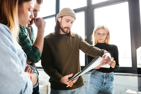 Picture of young serious colleagues standing in office holding notebook. Looking aside.