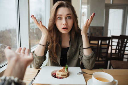 Indignant woman abput her friend while sitting and eating in cafeの写真素材