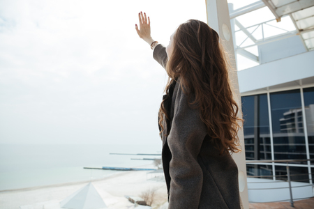 Young woman raising her hand to sun while walking near seaの写真素材