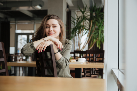 Smiling brunette woman looking camera while sitting in cafeの写真素材