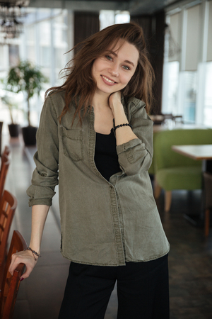 Woman standing in cafe leaning on chair and smilingの写真素材