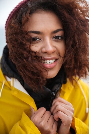 Portrait of smiling african curly young woman wearing yellow coat walking outdoors. Looking at camera.の写真素材