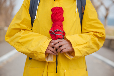 Vertical shot of closed red umrella in woman's hand near chestの写真素材