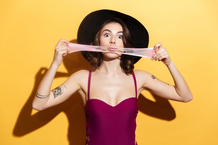 Portrait of a playful cute girl in swimsuit chewing bubble gum and having fun isolated over yellow backgroundの写真素材