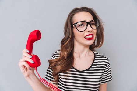 Image of confused young lady standing over grey wall holding phone. Looking at camera.の写真素材