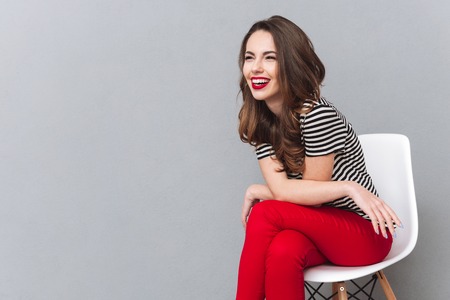 Image of laughing young lady sitting over grey wall posing. Looking aside.の写真素材