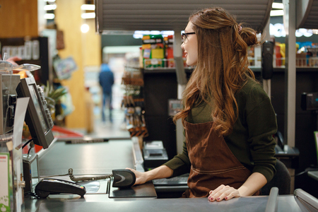 Picture of cashier woman on workspace in supermarket shop. Looking aside.の写真素材
