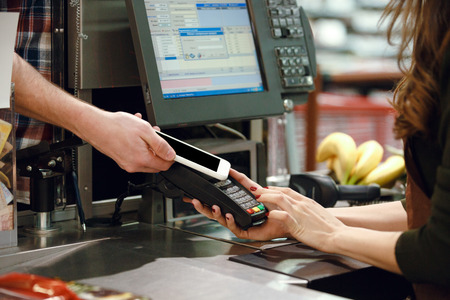 Cropped image of cashier woman on workspace in supermarket shop create payment with mobile phone app.の写真素材
