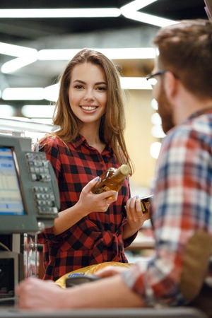 Image of smiling young lady standing in supermarket shop near cashier's desk. Looking at camera.の写真素材