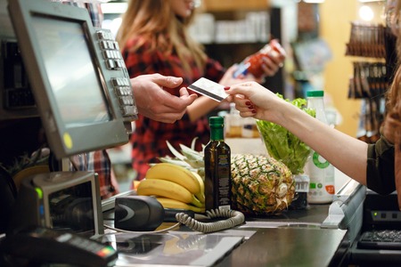 Cropped picture of young man gives credit card to cashier lady at workspace in supermarket.の写真素材