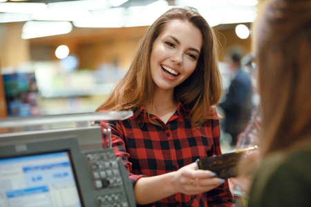 Image of smiling young lady standing in supermarket shop near cashier's desk. Looking aside.の写真素材